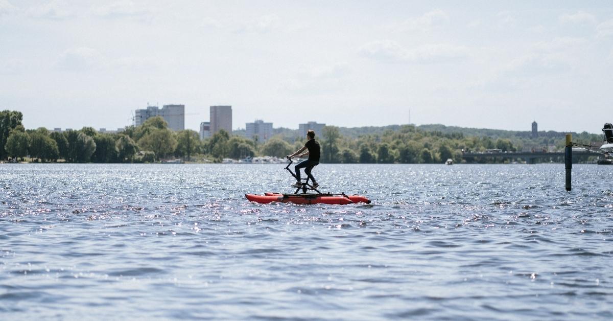 Ein Mann fährt auf einem Wasserfahrrad über einen See bei Sonnenschein.